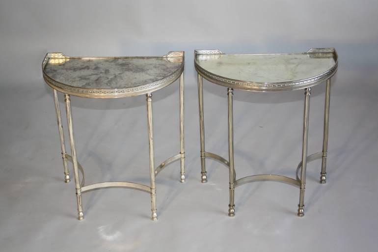 A pair of demi lune silver metal side tables with aged mirror glass tops, French